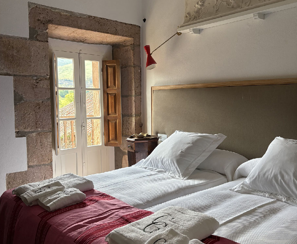 Habitación rústica con cama de matrimonio en Casa Guanes, destacando sus muros de piedra vista y vistas al paisaje de Cantabria.